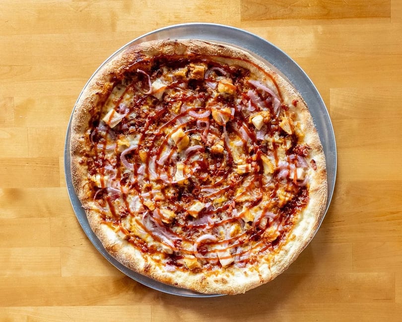 BBQ chicken pizza with red onions and a swirl of BBQ sauce on a wooden table.