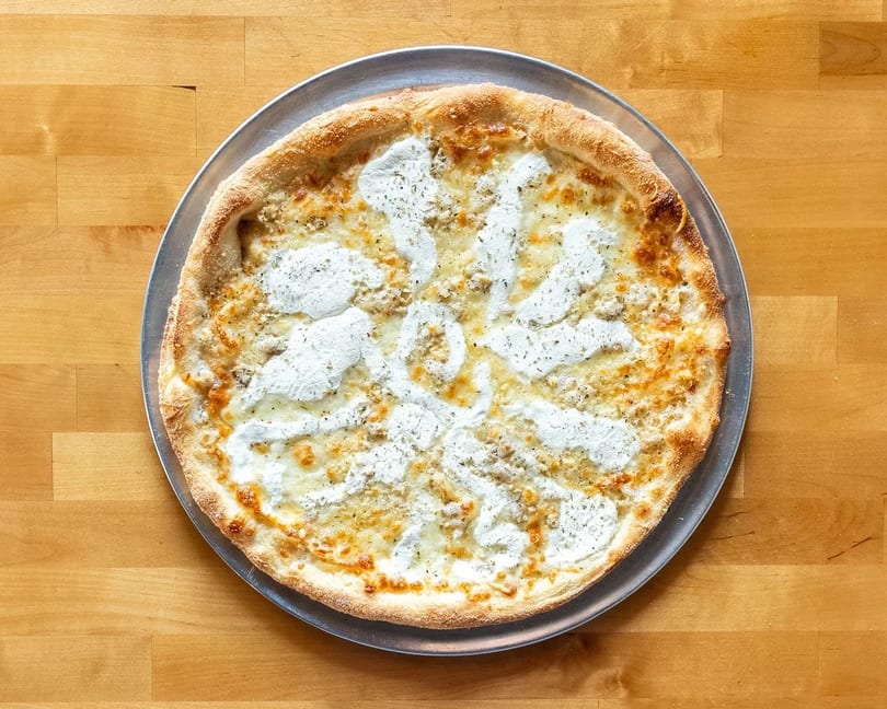 White pizza with ricotta cheese, mozzarella, and herbs on a metal pan, on a wooden table.